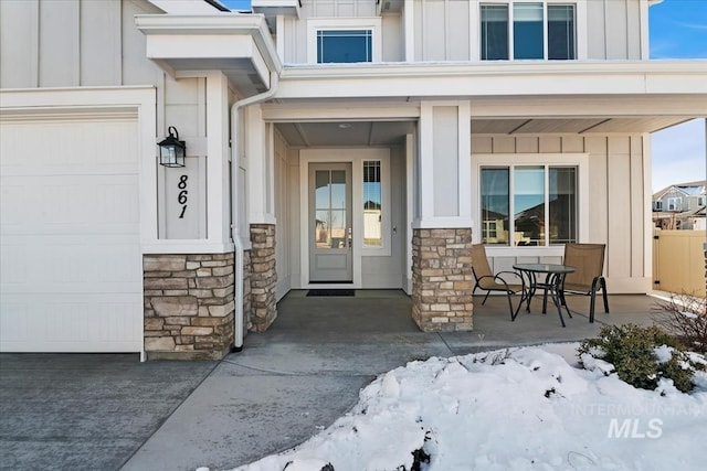 snow covered property entrance with a garage and covered porch