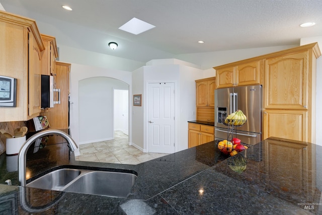 kitchen with light brown cabinetry, high end fridge, lofted ceiling with skylight, sink, and light tile patterned flooring