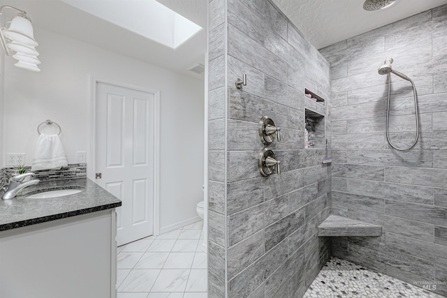 bathroom featuring a tile shower, vanity, a skylight, and toilet