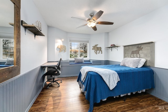 bedroom with ceiling fan, wooden walls, and dark wood-type flooring