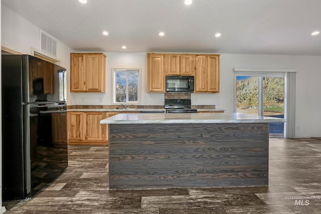 kitchen with light stone countertops, dark wood-type flooring, sink, black appliances, and a center island