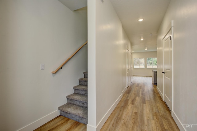 corridor with light wood finished floors, recessed lighting, stairs, and baseboards