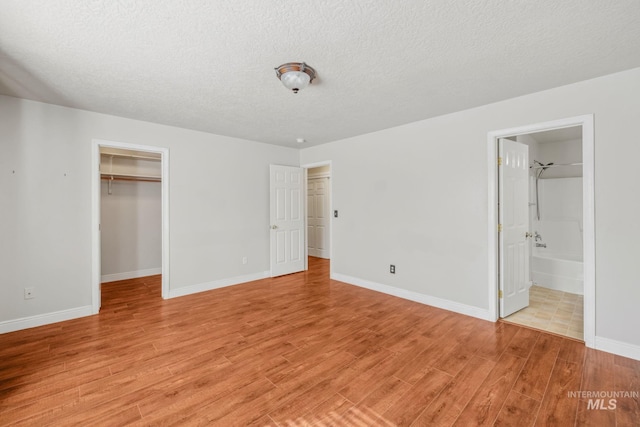 5101 Barkley Way, Caldwell, ID 83607 - unfurnished bedroom with light wood finished floors, a walk in closet, a textured ceiling, baseboards, and a closet