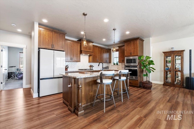 kitchen with dark wood finished floors, hanging light fixtures, a center island with sink, and appliances with stainless steel finishes