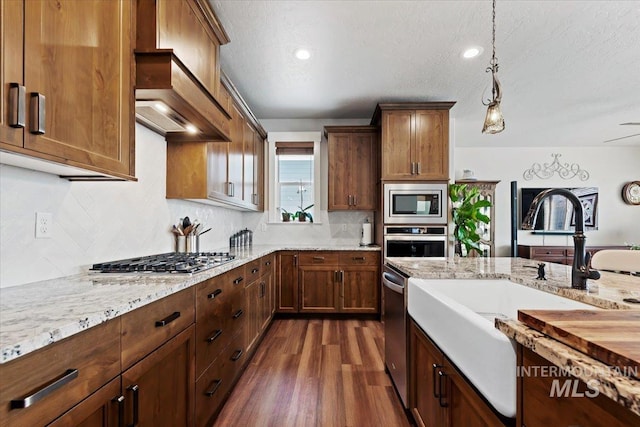 kitchen featuring light stone countertops, dark wood-style flooring, a sink, custom range hood, and appliances with stainless steel finishes