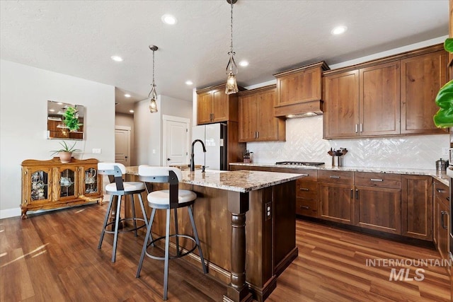 kitchen featuring stainless steel gas stovetop, a kitchen island with sink, dark wood-style flooring, and freestanding refrigerator