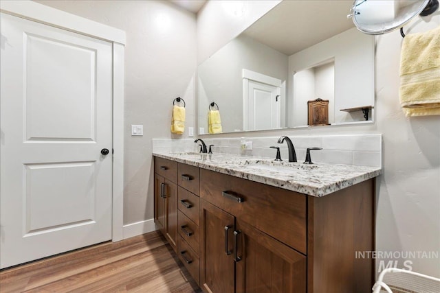 bathroom with double vanity, wood finished floors, baseboards, and a sink