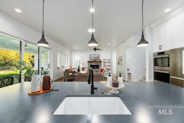 kitchen with a sink, dark countertops, stainless steel appliances, white cabinets, and a fireplace