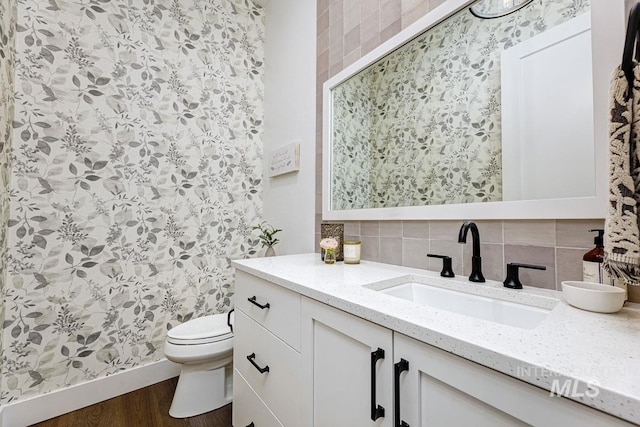 bathroom featuring vanity, toilet, wood finished floors, and backsplash