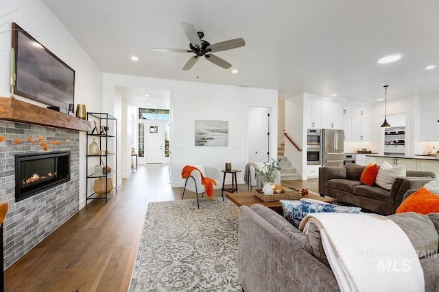 living area with wood finished floors, recessed lighting, ceiling fan, stairs, and a glass covered fireplace