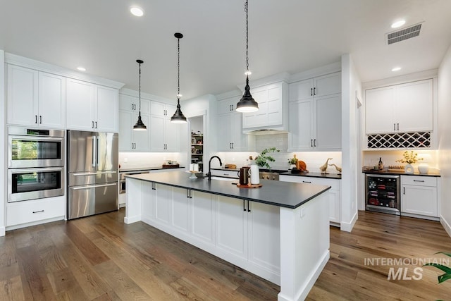 kitchen with beverage cooler, visible vents, a sink, stainless steel appliances, and dark countertops