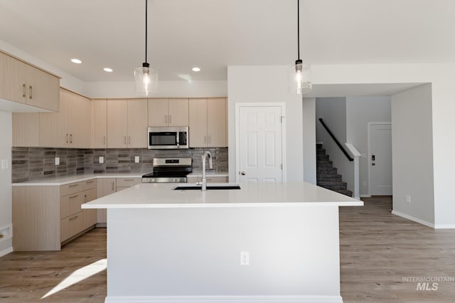 kitchen with stainless steel appliances, a kitchen island with sink, sink, and light brown cabinets