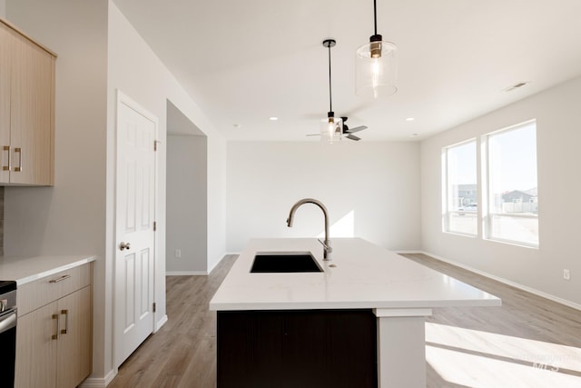 kitchen with pendant lighting, sink, light brown cabinetry, and a center island with sink