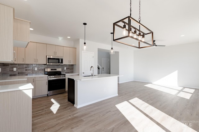 kitchen with sink, hanging light fixtures, an island with sink, stainless steel appliances, and backsplash