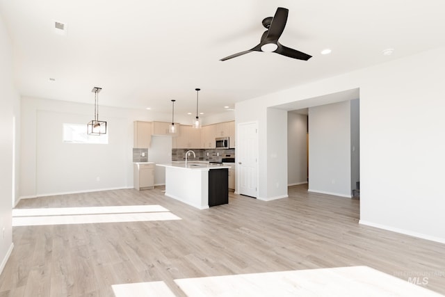 kitchen with sink, tasteful backsplash, hanging light fixtures, light wood-type flooring, and an island with sink