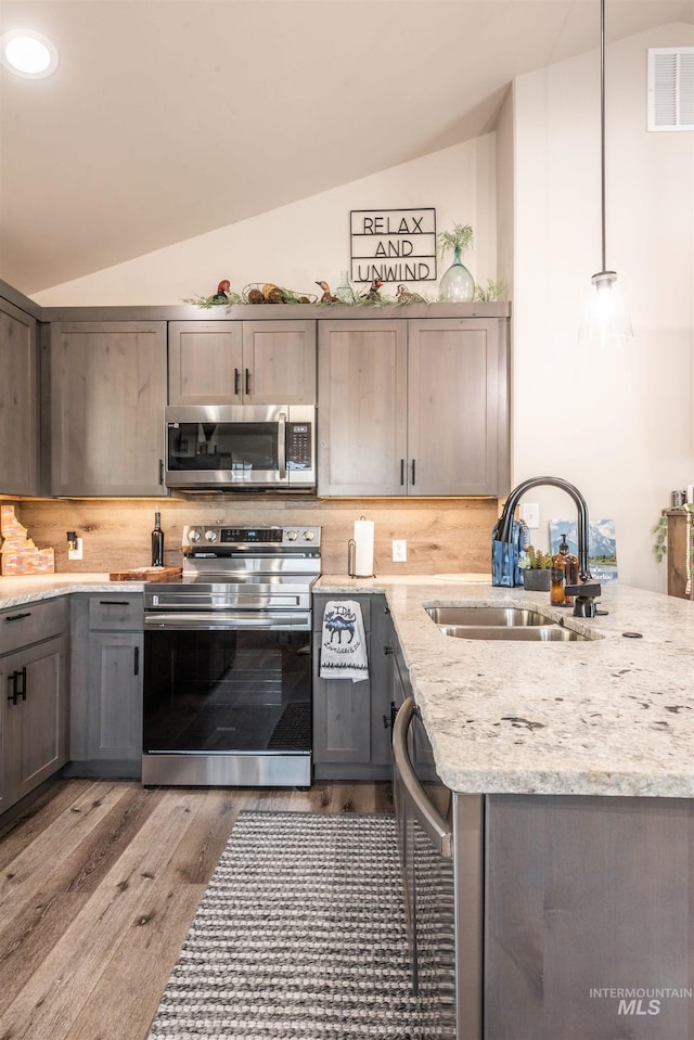 kitchen with pendant lighting, stainless steel appliances, lofted ceiling, and sink