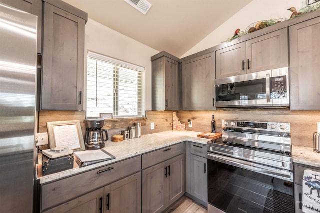 kitchen featuring light stone countertops, lofted ceiling, appliances with stainless steel finishes, and tasteful backsplash