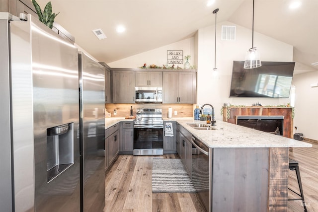 kitchen with tasteful backsplash, light stone counters, stainless steel appliances, sink, and pendant lighting