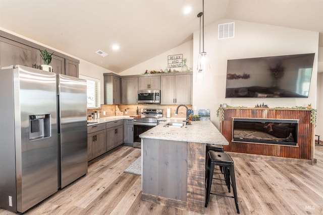 kitchen with backsplash, sink, hanging light fixtures, appliances with stainless steel finishes, and kitchen peninsula