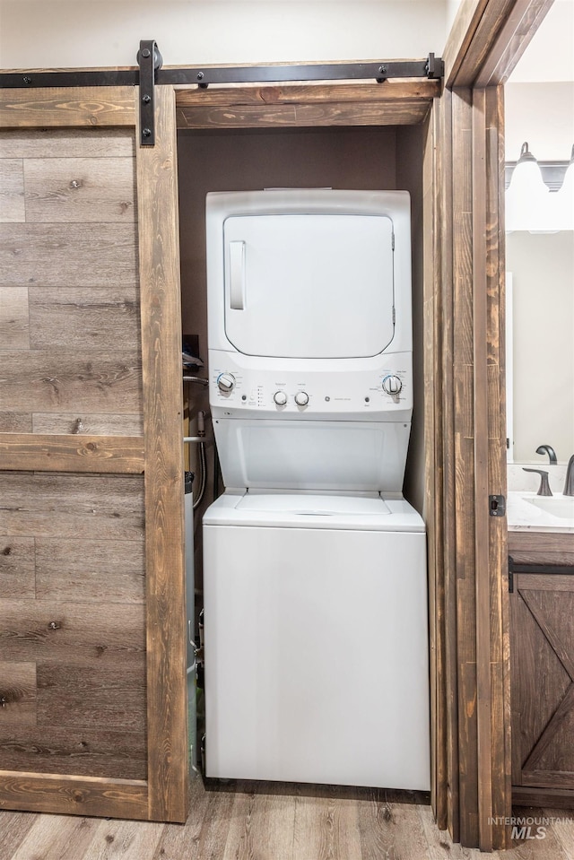 laundry room with a barn door, light hardwood / wood-style floors, stacked washer / drying machine, and sink