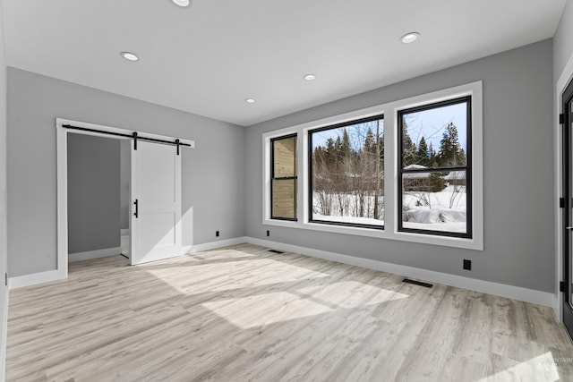 unfurnished bedroom with visible vents, a barn door, light wood finished floors, and baseboards