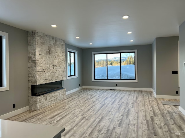 unfurnished living room with baseboards, recessed lighting, a fireplace, and light wood-style floors