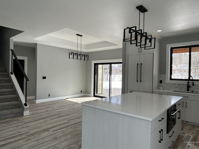 kitchen featuring a center island, a sink, baseboards, a raised ceiling, and light wood-style flooring