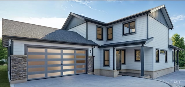 view of front facade featuring roof with shingles, stone siding, a garage, and concrete driveway