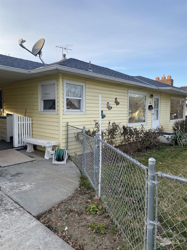 view of front of home with a shingled roof, a patio area, and fence