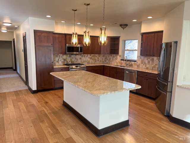 kitchen with a kitchen island, pendant lighting, sink, light stone counters, and stainless steel appliances