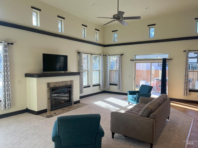 living room featuring a tiled fireplace, a towering ceiling, and ceiling fan