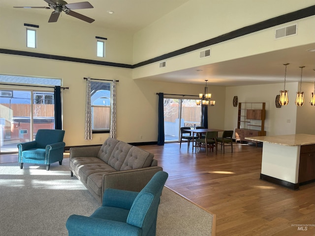 living room with a high ceiling, dark hardwood / wood-style floors, and ceiling fan with notable chandelier