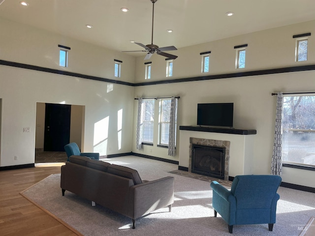 living room with ceiling fan, light hardwood / wood-style floors, a healthy amount of sunlight, and a high ceiling