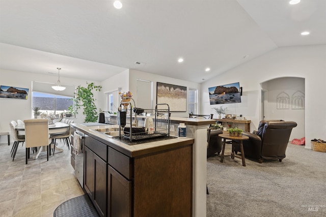 kitchen with light carpet, dark brown cabinets, vaulted ceiling, a kitchen island with sink, and pendant lighting