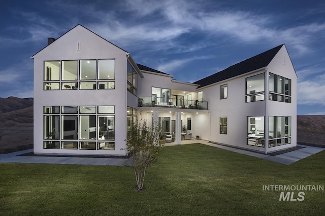 rear view of house with a patio area, a yard, a balcony, and stucco siding