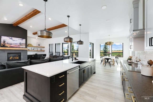 kitchen with stainless steel dishwasher, open floor plan, a sink, dark cabinetry, and light wood-style flooring