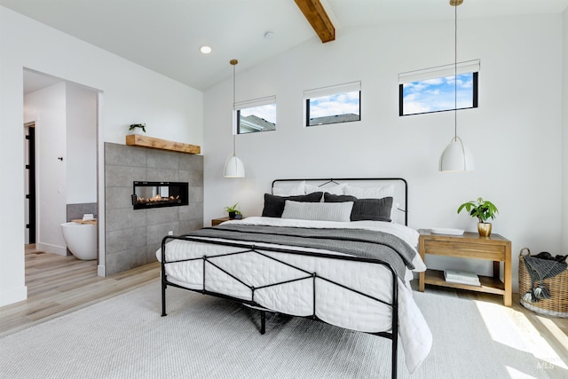 bedroom with light wood-style floors, a tile fireplace, and ensuite bath
