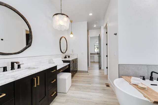 full bath with wood finished floors, vanity, a soaking tub, recessed lighting, and baseboards