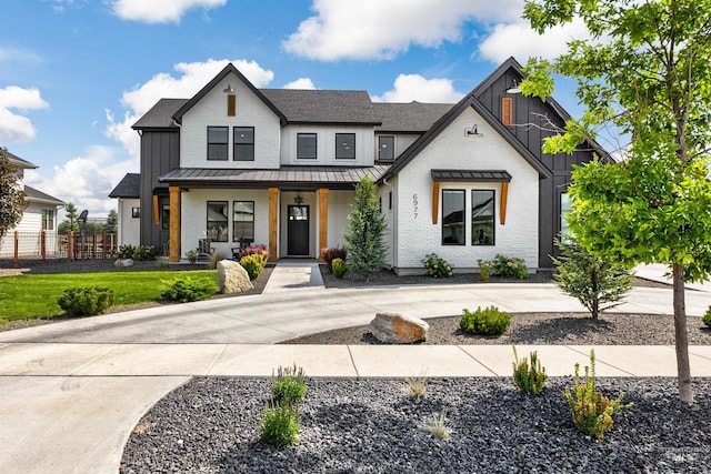 modern farmhouse featuring a standing seam roof, board and batten siding, a porch, and fence