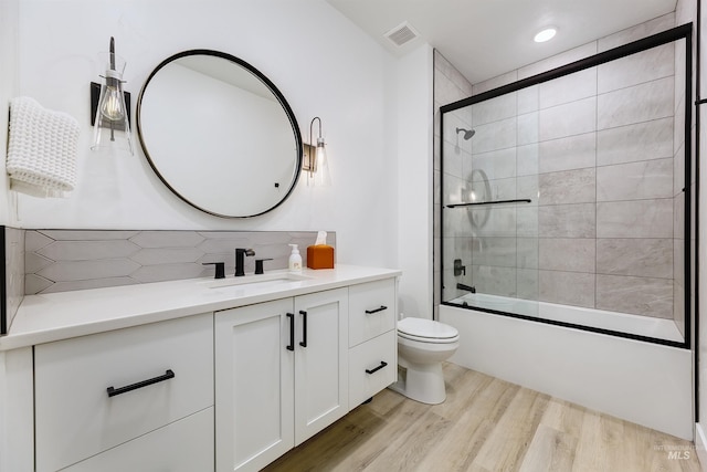 full bath featuring decorative backsplash, wood finished floors, toilet, vanity, and shower / bath combination with glass door