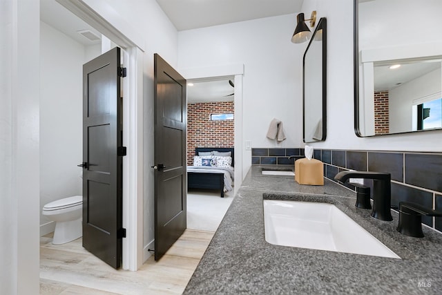 bathroom featuring connected bathroom, wood finished floors, toilet, and double vanity