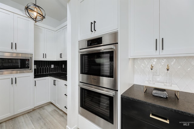 kitchen with appliances with stainless steel finishes, dark countertops, decorative backsplash, white cabinets, and light wood-style flooring