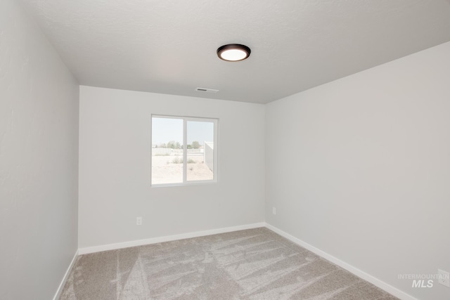 carpeted spare room featuring baseboards, visible vents, and a textured ceiling