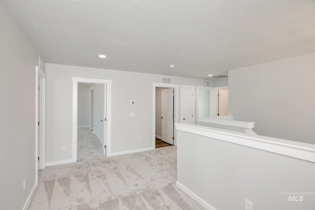 spare room with visible vents, a textured ceiling, baseboards, and carpet