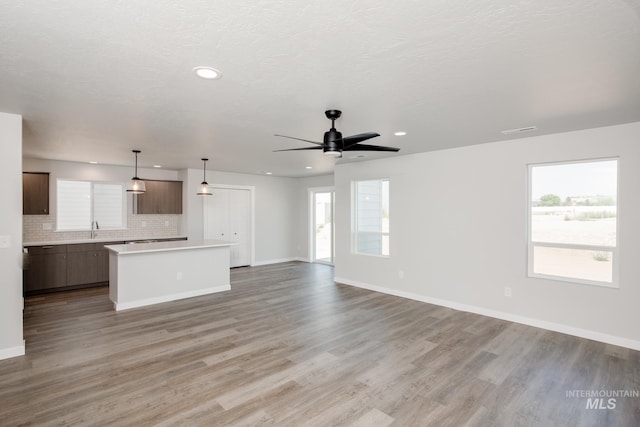 unfurnished living room with a sink, a wealth of natural light, a ceiling fan, and light wood finished floors