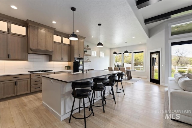 8749 W Suttle Lake Dr, Boise, ID 83714 - kitchen with a kitchen island with sink, light wood-type flooring, a kitchen bar, backsplash, and recessed lighting
