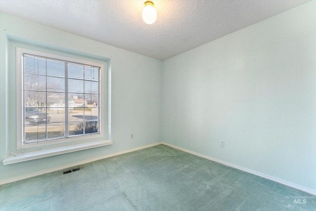 spare room with a textured ceiling, carpet, visible vents, and baseboards