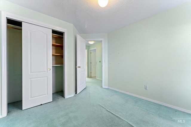 unfurnished bedroom featuring a closet, baseboards, a textured ceiling, and light colored carpet