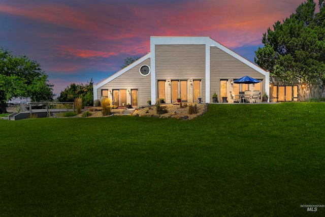 back house at dusk featuring a lawn and a patio