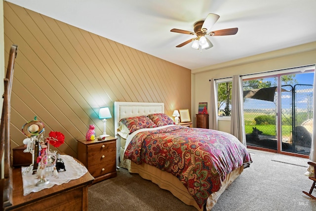 carpeted bedroom with access to outside, wood walls, and ceiling fan